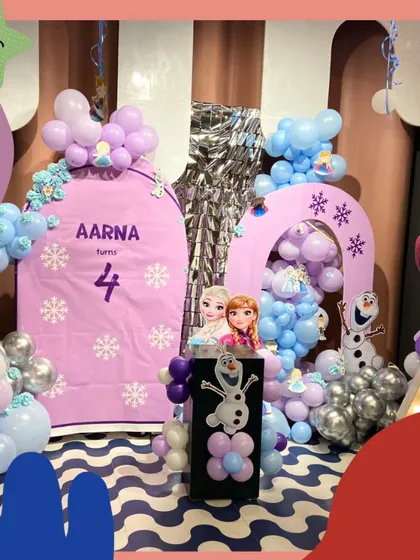 A magical Frozen-themed setup for Aarna's 4th birthday. The decorations include purple arches, snowflake details, and cutouts of Anna, Elsa, and Olaf.