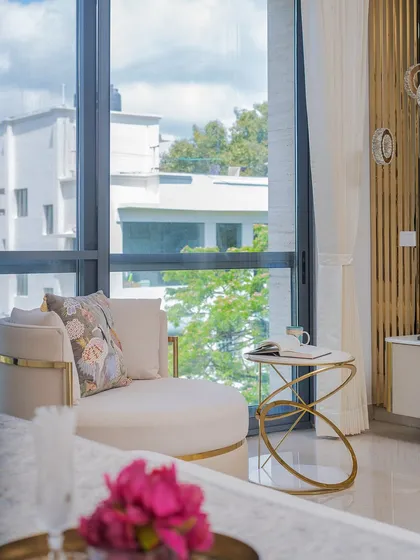 A thoughtfully styled corner featuring a curved accent chair with a metal trim and a designer side table in high-gloss gold. The soft floral cushion adds a touch of contrast and comfort.