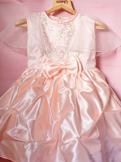 A closer view of this peach satin party dress, highlighting the delicate floral embroidery on the bodice and the sheer, wing-like sleeves that add a touch of whimsy.