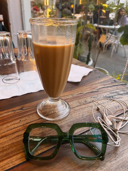 An aesthetic shot of cold coffee and my glasses on a wooden table, capturing a simple weekend vibe.