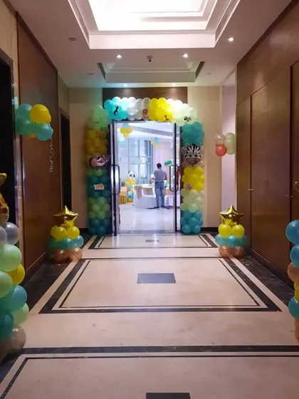 An entrance to a jungle-themed party in a hotel corridor. A colorful balloon arch and giraffe-themed balloon pillars welcome guests to the celebration.
