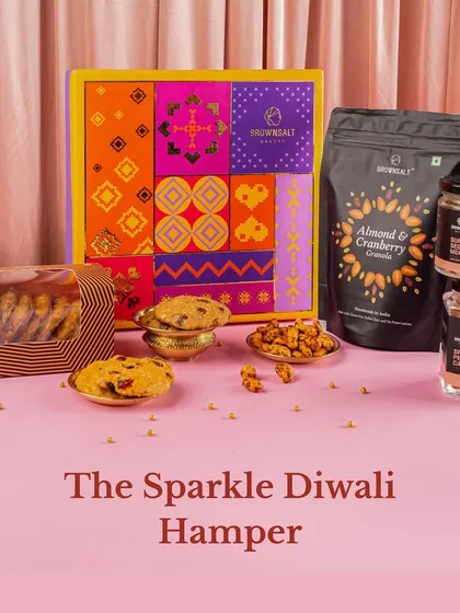 The Sparkle Diwali Hamper is all about festive joy. This beautifully styled shot shows the vibrant packaging alongside the contents, including our Almond & Cranberry Granola, assorted cookies, and jars of spiced nuts and seeds.