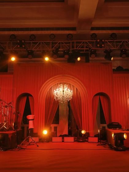 The stage for the evening's entertainment, washed in a warm red glow. The arched backdrop and crystal chandeliers add a touch of classic elegance to the modern monochromatic theme.