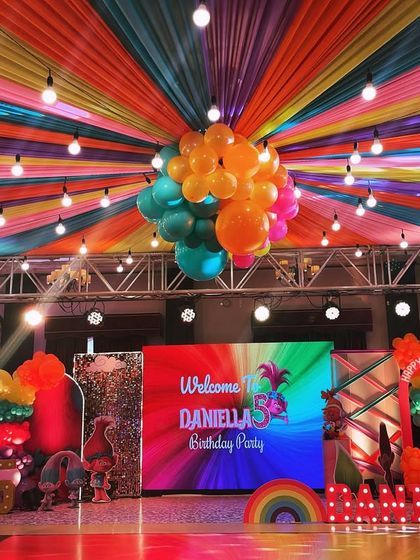 The complete stage setup for Daniela's 5th birthday Trolls party, featuring a large LED screen, character cutouts, and a rainbow of balloon decorations.