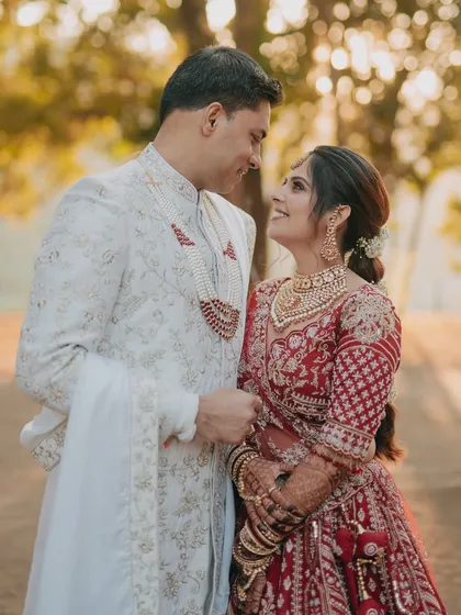 A classic couple portrait where the bride and groom share a look of love. The natural, outdoor setting provides a beautiful, soft backdrop for their traditional red and white outfits.