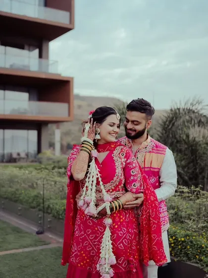 This couple looks picture-perfect. The bride's floral kalire, crafted with white flowers and pink buds, adds a touch of grace to her vibrant pink bandhani outfit.