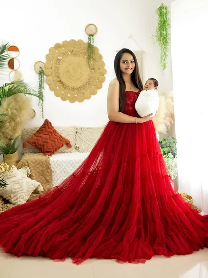 A full-length portrait of the mother in a striking red dress, proudly holding her swaddled newborn.