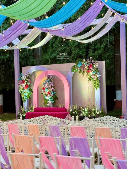 A pastel-themed stage with a bright pink sofa, framed by arches and floral arrangements.
