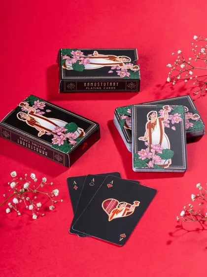 A vibrant flat lay of Namostutay playing cards against a bold red background. The styling with delicate white flowers provides a beautiful contrast and highlights the product's artistic design.