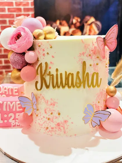 A beautiful personalized cake with pink splatter details, butterflies, and a block showing the date and time of birth.