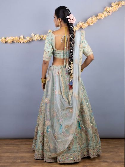 The back view highlights the beautiful hairstyle and the detailed embroidery on the back of the blouse, as well as the playful tassels on the skirt.