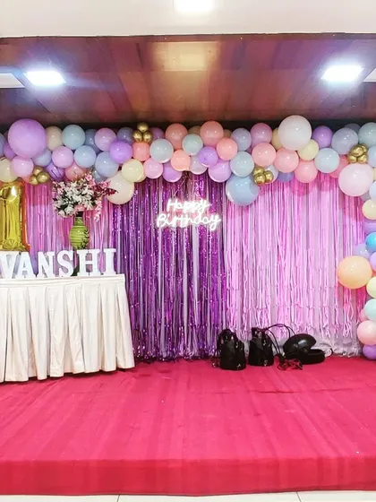 A large-scale pastel balloon garland for a first birthday celebration at a hall. The soft colors, combined with a shimmer curtain and a neon sign, create an elegant and grand backdrop for the cake table.