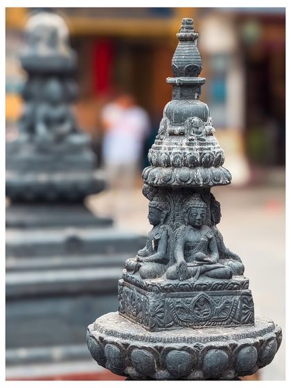 Another detailed shot of a miniature stupa, with the blurred background hinting at the bustling city life.
