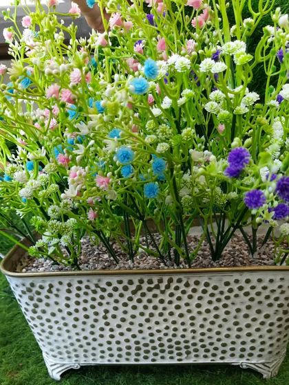 This metal bucket-style planter in a distressed white finish is filled with colourful artificial baby's breath flowers. It's a lovely, rustic piece that can brighten up any tabletop or corner.