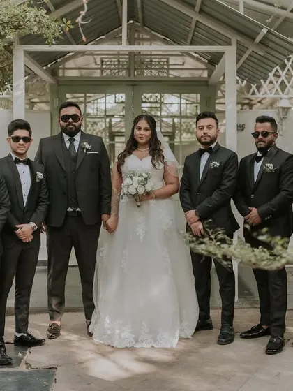 A bride and her groomsmen pose for a classic group photo. The clean, white architecture of the cottage provides a great contrasting background for their dark suits.