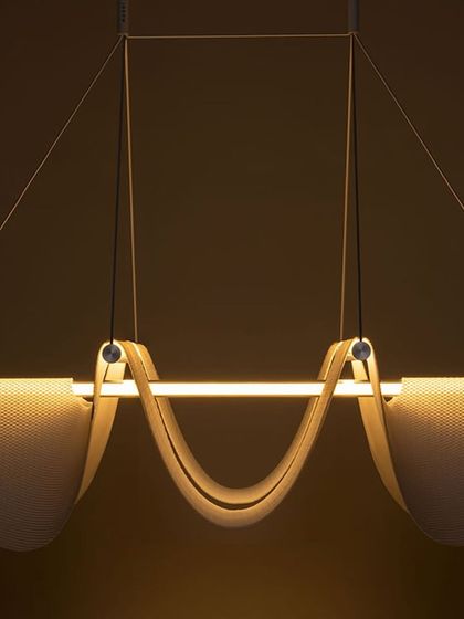 A close-up studio shot of the Drape Light, highlighting the gentle curve of the shade and the warm, linear light source it contains.