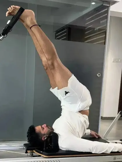 Varun Dhawan performing an inversion on the Reformer. This advanced move is excellent for spinal decompression and building core strength, demonstrating the versatility of Pilates for men.