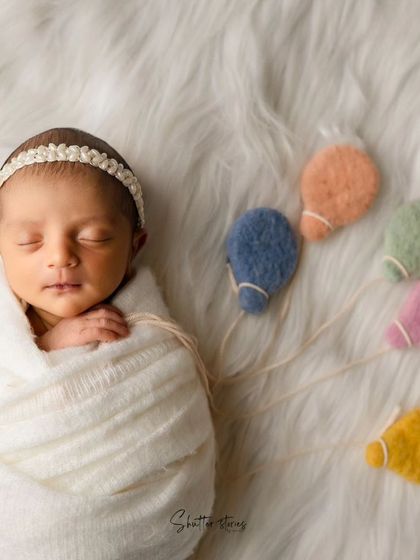 A creative variation on the white theme, with the newborn holding a string of colorful felt balloons.