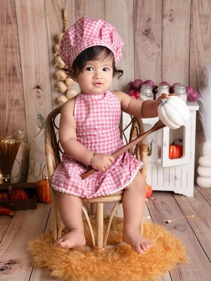 Another shot of our adorable little chef, this time sitting on a tiny chair. The wooden backdrop and rustic props complete this charming kitchen-themed portrait.