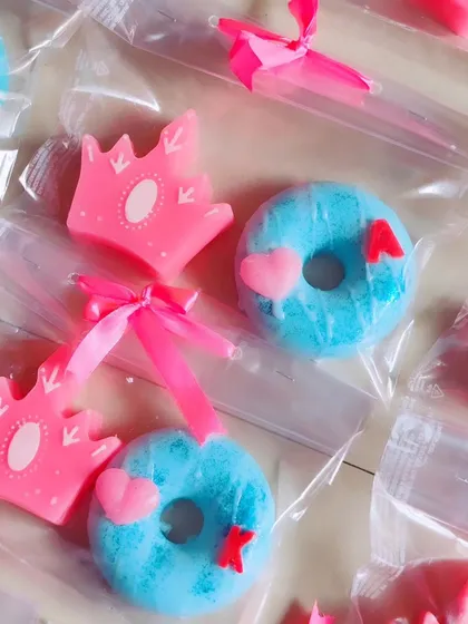 A set of return favors for a princess or superhero party, featuring crown soaps and donut soaps with initials.