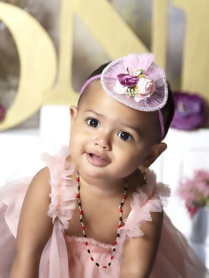 A sweet moment from a first birthday photoshoot. This little girl, in her pink dress, is ready for her cake smash in a lovely floral garden setting.