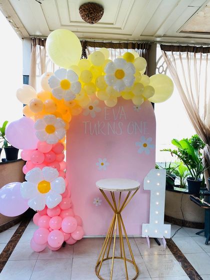 A lovely daisy-themed first birthday party with a pink backdrop and a colorful balloon arch.