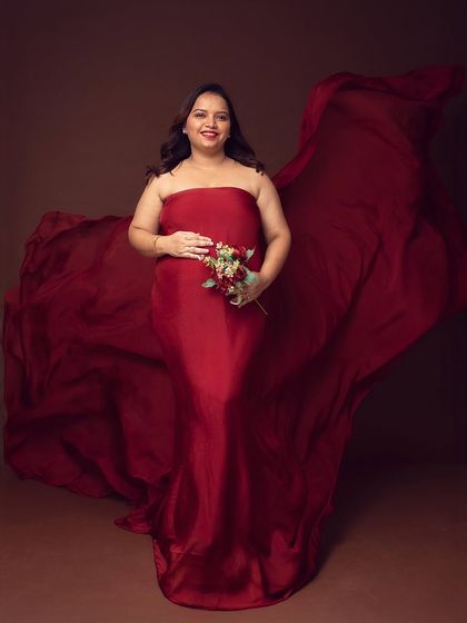 The power of red. This portrait features a gorgeous mom-to-be in a flowing red fabric drape, holding a bouquet that complements the rich color. The dark background makes the color pop.