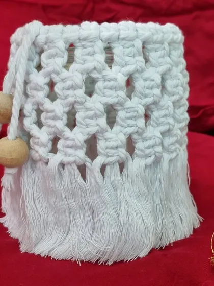 A white macrame jar cover with wooden beads, styled against a red background.