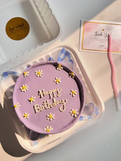 A classic "Happy Birthday" bento cake in a beautiful lavender shade, decorated with small, hand-piped daisies for a fresh and cheerful look.