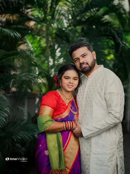 A classic portrait of the couple standing together amidst greenery. The bride's vibrant, multi-colored saree stands out beautifully in this timeless shot.