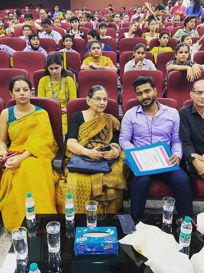 Sitting with fellow judges and faculty at a school auditorium for a dance competition.