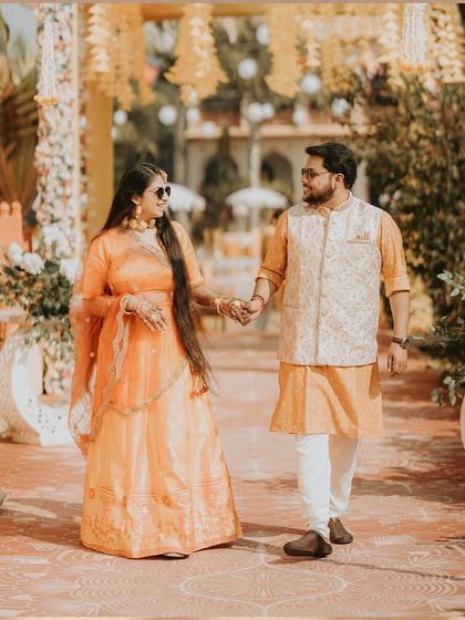 The bride and groom, dressed in beautiful shades of orange, walk hand-in-hand through their beautifully decorated Haldi venue in Orchha, showcasing a destination wedding celebration.
