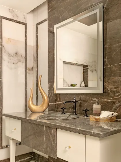 This neo-classical powder room combines intricate detailing with modern comforts. The dark marble countertop and ornate basin are paired with classic wall molding for a lavish and opulent feel.
