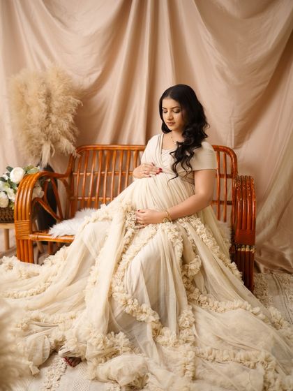 A quiet moment for the mother-to-be, seated on the rattan bench. The flowing cream gown and pampas grass create a beautifully textured and serene boho portrait.
