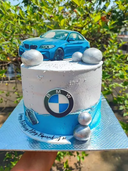 Of dreams and passion. A sleek BMW-themed cake for a car enthusiast, featuring a toy car topper, the BMW logo, and a silver and blue color scheme.