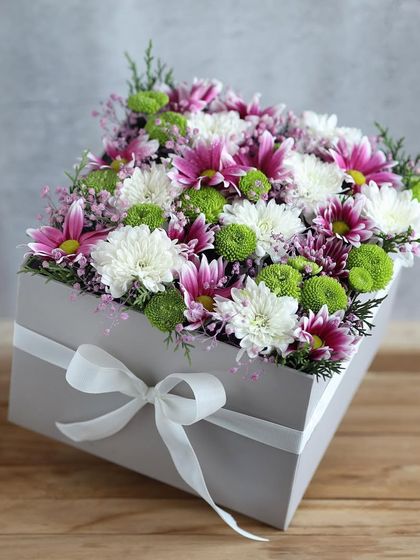 A modern grey box overflowing with beautiful purple and white chrysanthemums, a sophisticated floral gift for Women's Day.