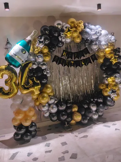 A stylish black, silver, and gold ring decoration for a 34th birthday, featuring a champagne bottle foil balloon.