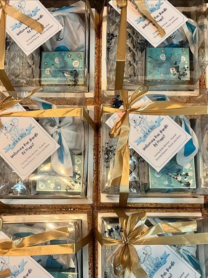 A view of a bulk order for baby announcement hampers. Each gift is packed in a clear box with a gold ribbon and a personalized "It's a Boy" tag.