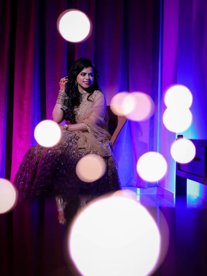 A portrait of a woman seated, with bokeh from fairy lights in the foreground, creating a magical and colorful effect.