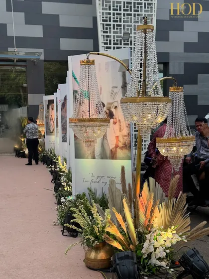 A unique entrance walkway lined with large photo panels of the couple, interspersed with elegant chandeliers on stands and pampas grass arrangements.
