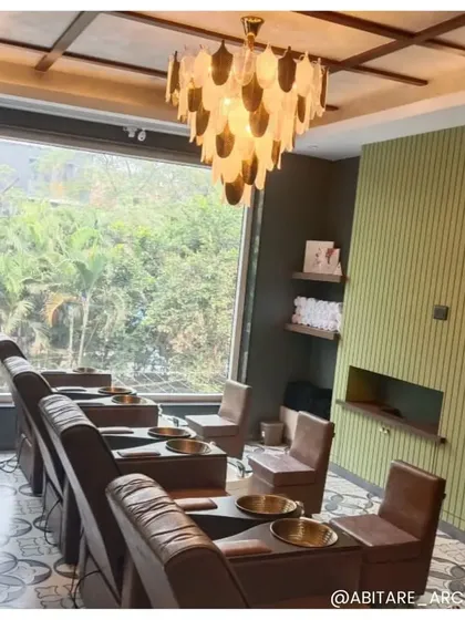 A view of the salon's pedicure area, overlooking lush greenery through a large window. The combination of natural light, a unique chandelier, and comfortable seating creates a tranquil oasis for clients to unwind.