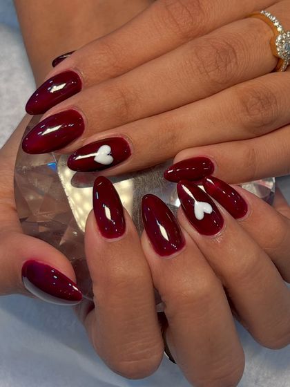 Another angle of the burgundy heart nails, held against a crystal to showcase their glossy finish and the perfect almond shape.