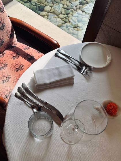 A quiet moment during lunch service at Indian Accent. The natural light, crisp white tablecloth, and elegant glassware create a serene and sophisticated atmosphere for a midday meal.