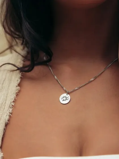 A woman wearing a silver-toned round pendant with a custom design. This image shows the delicate size and placement of the pendant for everyday wear.