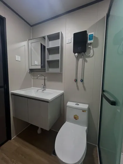 A well-appointed bathroom in one of our container homes. It includes a modern vanity with storage, a mirrored cabinet, and an efficient water heater, showcasing our attention to practical details.
