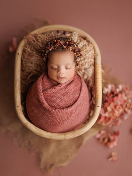 I love preserving these fleeting moments. This overhead shot in a wooden bowl shows off the beautiful wrap and the baby's peaceful expression, surrounded by coordinating flowers.