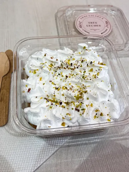 Our famous Tres Leches, now available in an eggless version. This photo shows our light, airy sponge soaked in three kinds of milk, topped with whipped cream and a sprinkle of pistachios, packaged and ready for you to enjoy.