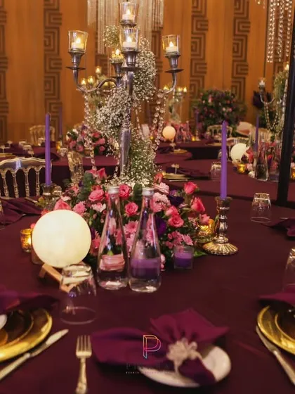 A closer look at the regal tablescape. The combination of gold charger plates, deep purple linens, and a centerpiece of glowing orbs and florals creates a truly luxurious dining setting.