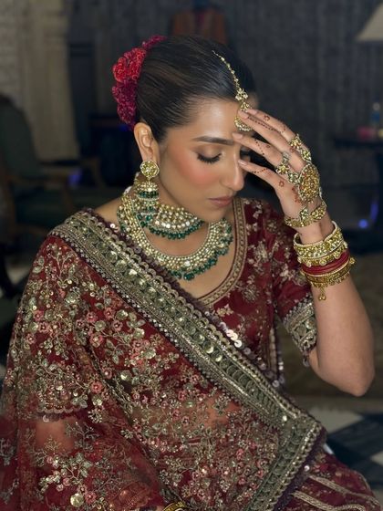 A candid moment of the bride, Ayushi, looking effortlessly stunning. Her makeup features warm tones and a subtle glow, complementing her deep red Sabyasachi lehenga and the intimate, regal setting of her wedding.