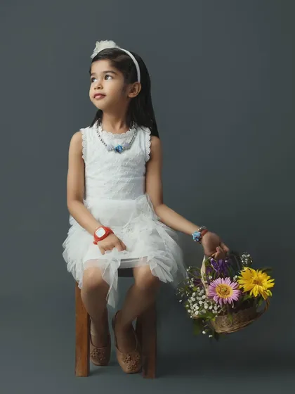 A beautiful portrait of a young girl in a white dress, holding a basket of flowers, as part of her family's studio session.